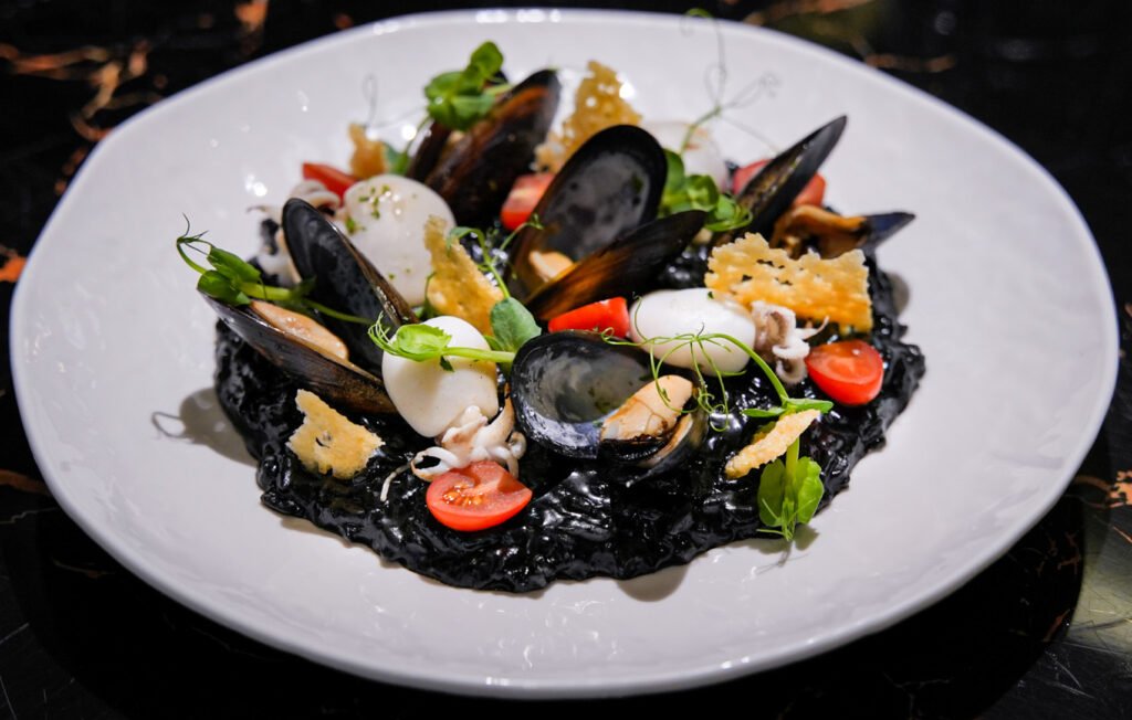 Squid Ink Seafood Risotto, creamy arborio rice infused with the rich, briny depth of squid ink. Mussels and baby cuttlefish, with notes of garlic and aromatic herbs, sprinkled with grated Parmesan and olive oil. A signature dish at Giglio Restaurant, Gourmet Street Lalaport BBCC