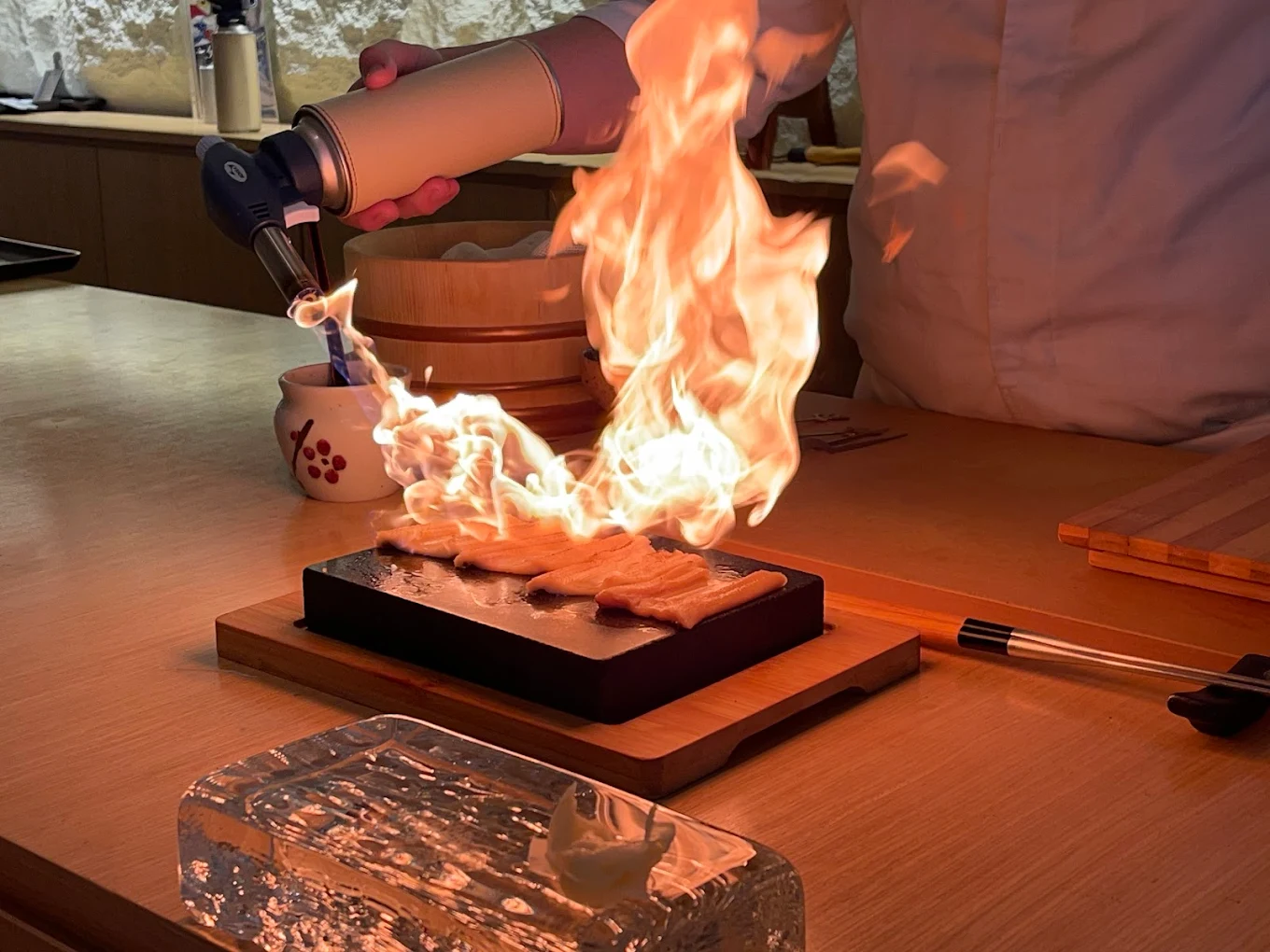 The chef at Sushi Yoshi Omakase, LaLaport BBCC is preparing Aburi sushi, where a blowtorch or searing technique is used to partially cook the sushi, adding a smoky flavour and enhancing the texture of the ingredients. This technique, called "aburi," means "flame-seared" and involves gently searing the surface of the fish to create a contrasting texture and flavour.