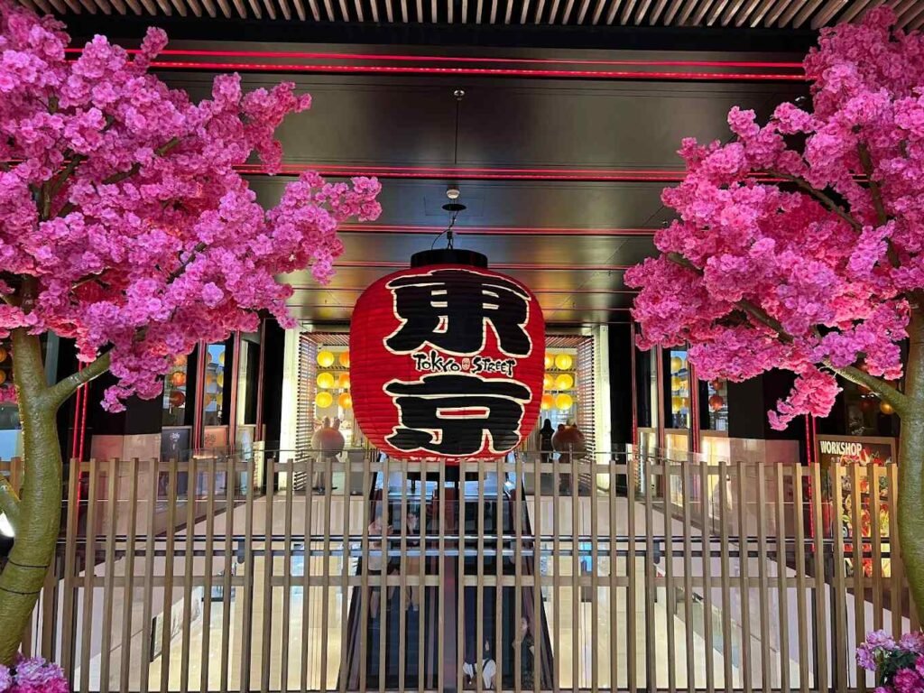 The vibrant red chochin Asakusa lantern, reminiscent of the Kaminarimon Thunder Gate at Senso-ji Temple, flanked by two cherry blossom trees at Tokyo Street Pavilion Kuala Lumpur.