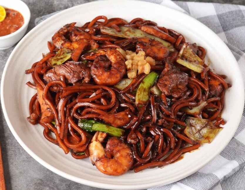 The Signature Hokkien Mee is a iconic Petaling Street noodle dish made with thick yellow noodles, stir-fried in a rich dark soy sauce over high heat to achieve a distinctive savory, smoky "wok hei" flavor, often topped with crispy pork lard. Available at KL Hokkien Mee stall at Food Place, a non-Halal food court in Pavilion KL, Bukit Bintang.