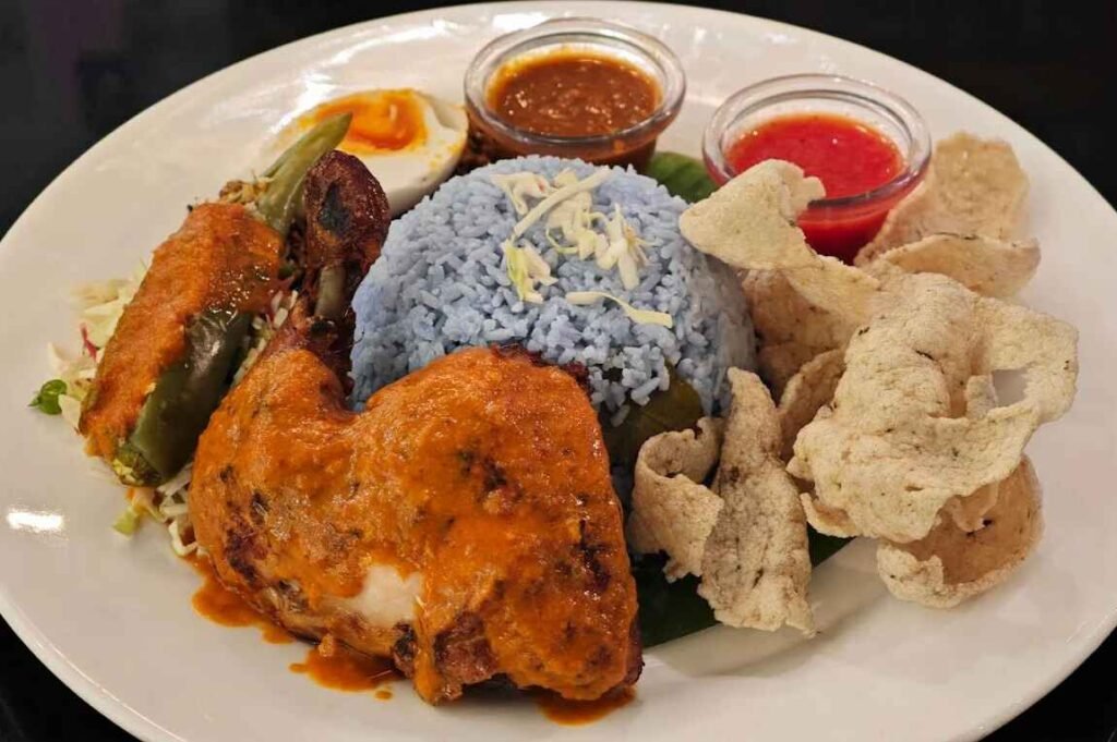 Nasi Kerabu, a signature dish at Serai, features blue-tinted rice served with ayam percik, salted egg, ulam, solok lada, keropok ikan accompanied with budu sauce.