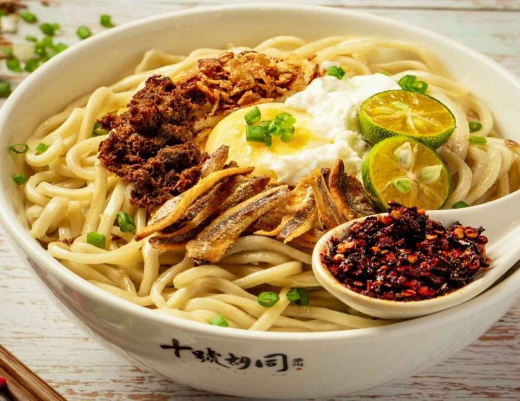 A bowl of Kin Kin’s famous Chili Pan Mee, a spicy variation of the Hakka noodle dish at Lot 10 Hutong, served with springy handmade noodles topped with minced pork, crispy anchovies, fried shallots, a soft-poached egg, and a side of fiery house-made dry chili flakes.