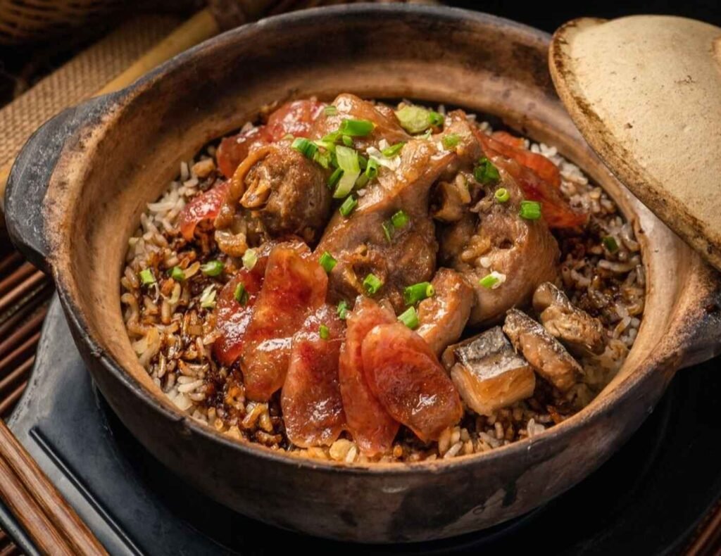 A steaming hot claypot of Zhun Kee's signature Claypot Chicken Rice With Salted Fish from Lot 10 Hutong, featuring tender marinated chicken wings, fragrant rice, glistening Chinese sausage slices, and chunks of savory salted fish, promising a crispy, golden crust at the bottom.