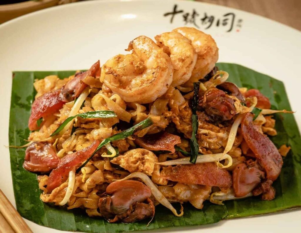 Penang Duck Egg Char Kuey Teow from Secret Penang Cafe at Lot 10 Hutong, featuring wok-fried flat rice noodles with Chinese sausages, prawns, bean sprouts, garlic chives, and a duck egg, cooked over charcoal for intense wok hei and rich, creamy flavour.