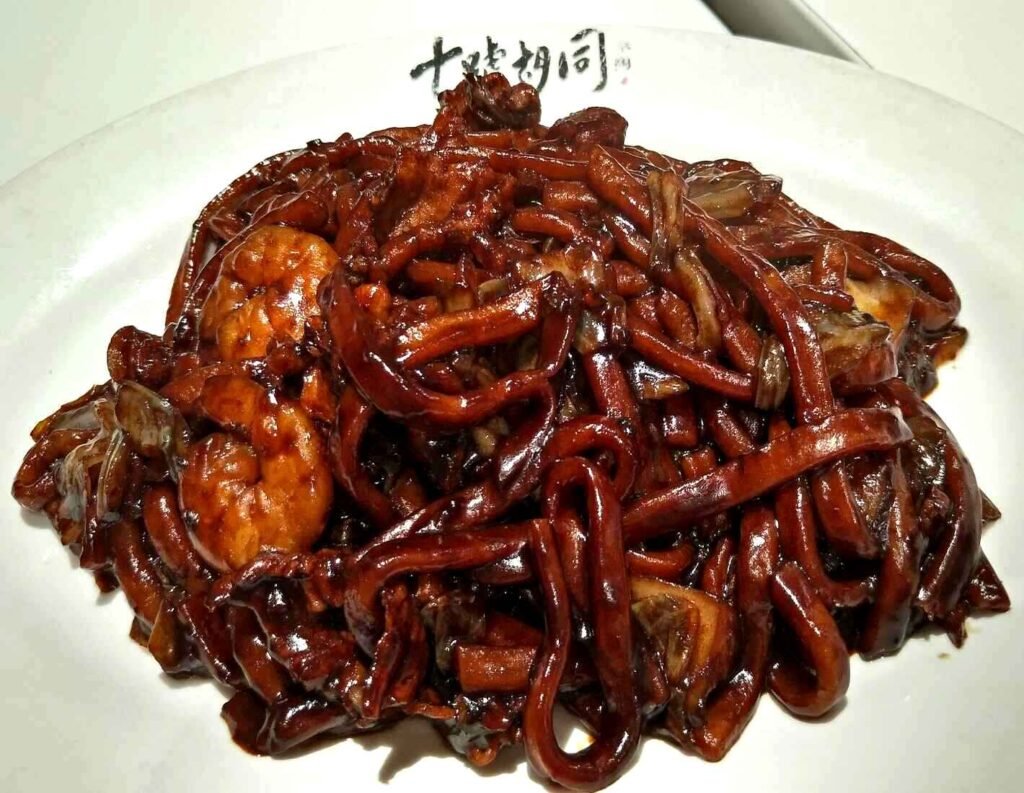 Hokkien Mee is a stir-fried noodle dish that consists of thick yellow noodles, which are stir-fried with prawns, pork belly, and dark soy sauce. A signature dish at Kim Lian Kee in Lot 10 Hutong, it is known for its umami-rich flavours and is served with sambal (a spicy chili paste), and crispy pork lard on the side.