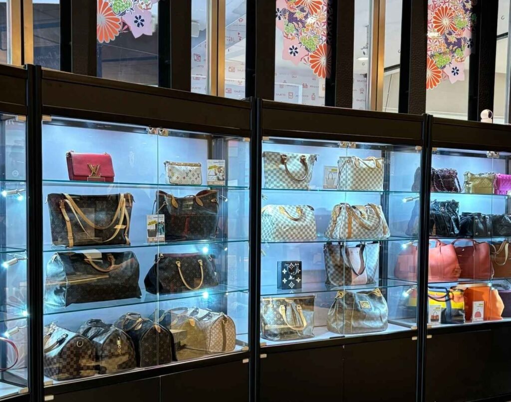 A brightly lit display of pre-loved luxury handbags from iconic brands like Louis Vuitton, showcased in black glass display cases at the Attic House, a handbag shop at The Design, Lower Ground Floor, Isetan The Japan Store Lot 10, Bukit Bintang, Kuala Lumpur.