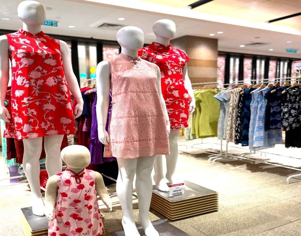 Modern cheongsam dresses for women and children displayed on mannequins at Cynthia Tang, featuring vibrant red floral prints and soft pastel designs. Located at The Design, Lower Ground Floor, Isetan The Japan Store Lot 10, Bukit Bintang, Kuala Lumpur.