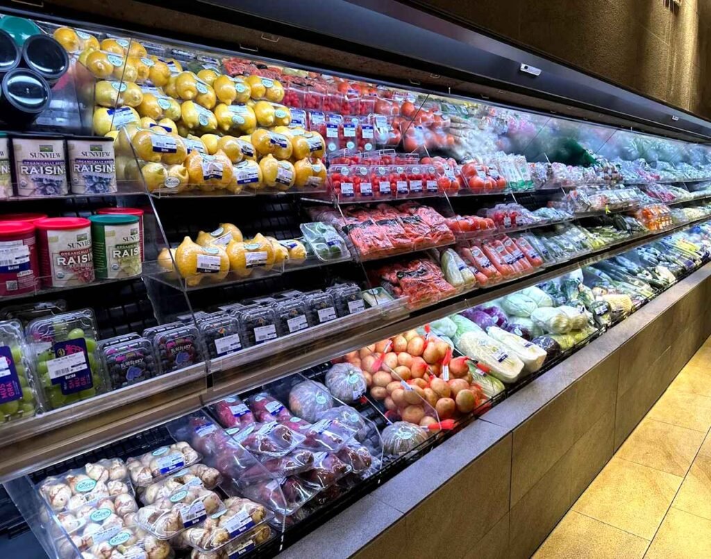 The fresh produce section shelves displaying Sunview Organic Raisins, Korean pears, red cherry tomatoes, medium round tomatoes, baby carrots, whole carrots, Japanese cucumbers, English cucumbers, Japanese long onions (negi), leeks, red chilies, mini orange sweet peppers, enoki mushrooms, mixed mushrooms, napa cabbage, Chinese cabbage, green cabbage, red cabbage, spring onions, leafy greens, Shine Muscat grapes, blueberries, arrowhead bulbs (ci gu), Japanese sweet potatoes (satsumaimo), beetroots, kabocha pumpkin, potatoes, along with many more fresh fruits and vegetables at The Market's Groceries section, located on the Lower Ground Floor of Isetan The Japan Store Lot 10, Bukit Bintang, Kuala Lumpur.