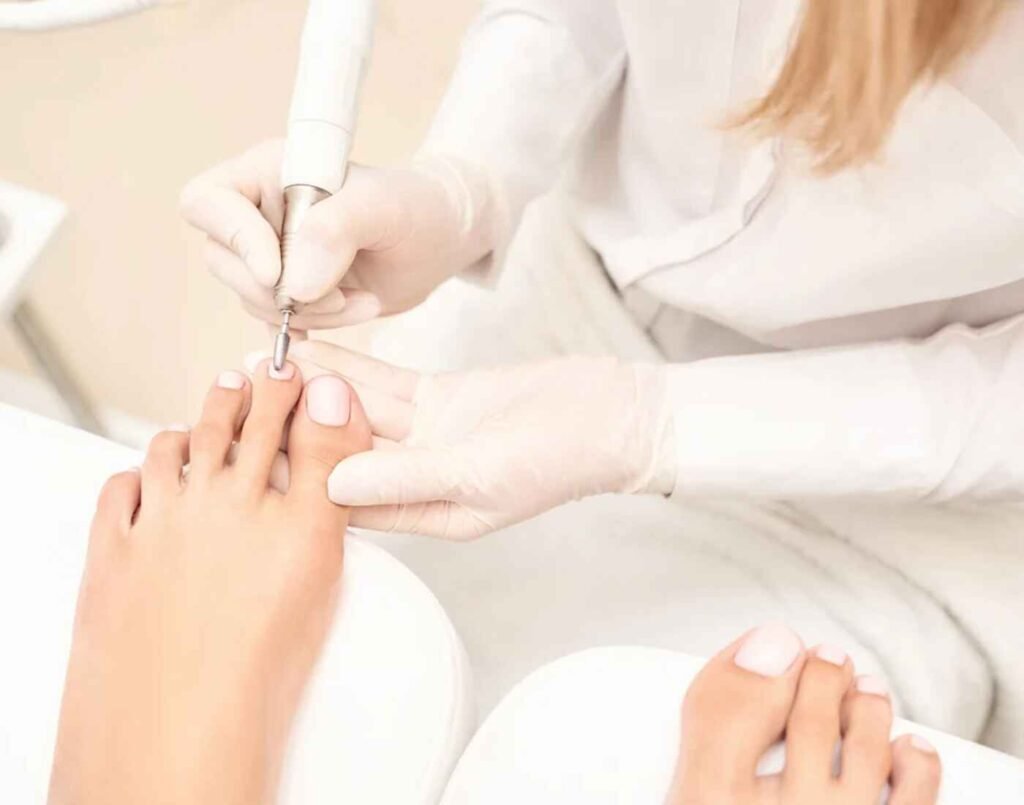 A close-up shot of a professional nail technician performing a pedicure on a woman's foot at Shyunmija, a premium nailory known for their immaculate nails and pampering hand and feet spa treatments. The manicurist, wearing white gloves, uses a nail drill to carefully shape the toenail, emphasizing the precision and hygienic standards of the treatment. Located at The Wellness, Second Floor, Isetan The Japan Store Lot 10, Bukit Bintang, Kuala Lumpur.
