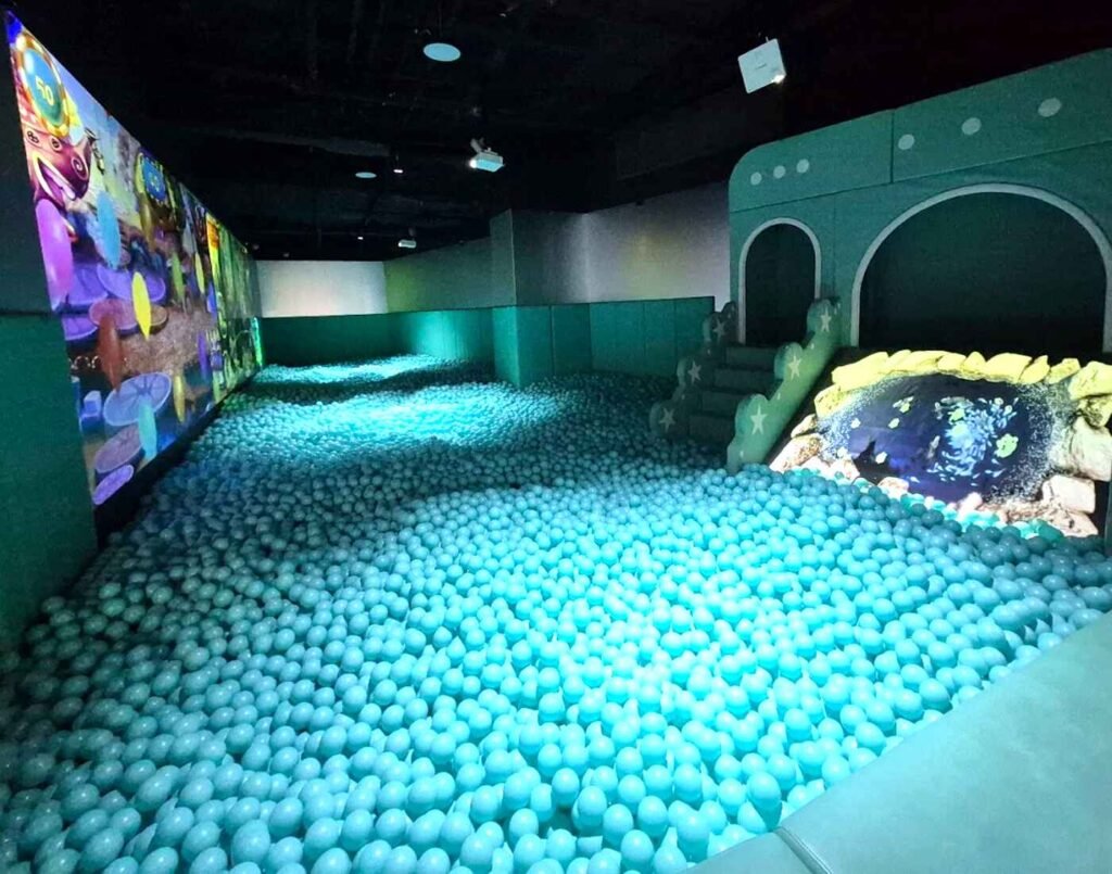A vast room filled with thousands of light blue plastic balls creates a dreamy ball pit, enhanced by digital wall projections and soft lighting that transform the space into a calming, immersive playground for children and parents at Space & Time Cube, The Amusement, Third Floor, Isetan The Japan Store Lot 10, Bukit Bintang, Kuala Lumpur.
