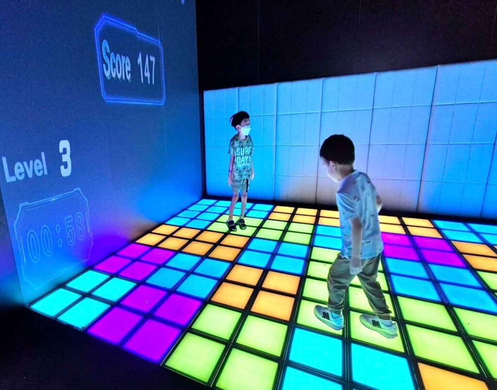 Children playing the Cube Puzzle, hopping onto designated colour tiles on the glowing LED floor to score points as the projected scoreboard updates in real time. This immersive playground for children is located in Space & Time Cube, The Amusement, Third Floor, Isetan The Japan Store Lot 10, Bukit Bintang, Kuala Lumpur.