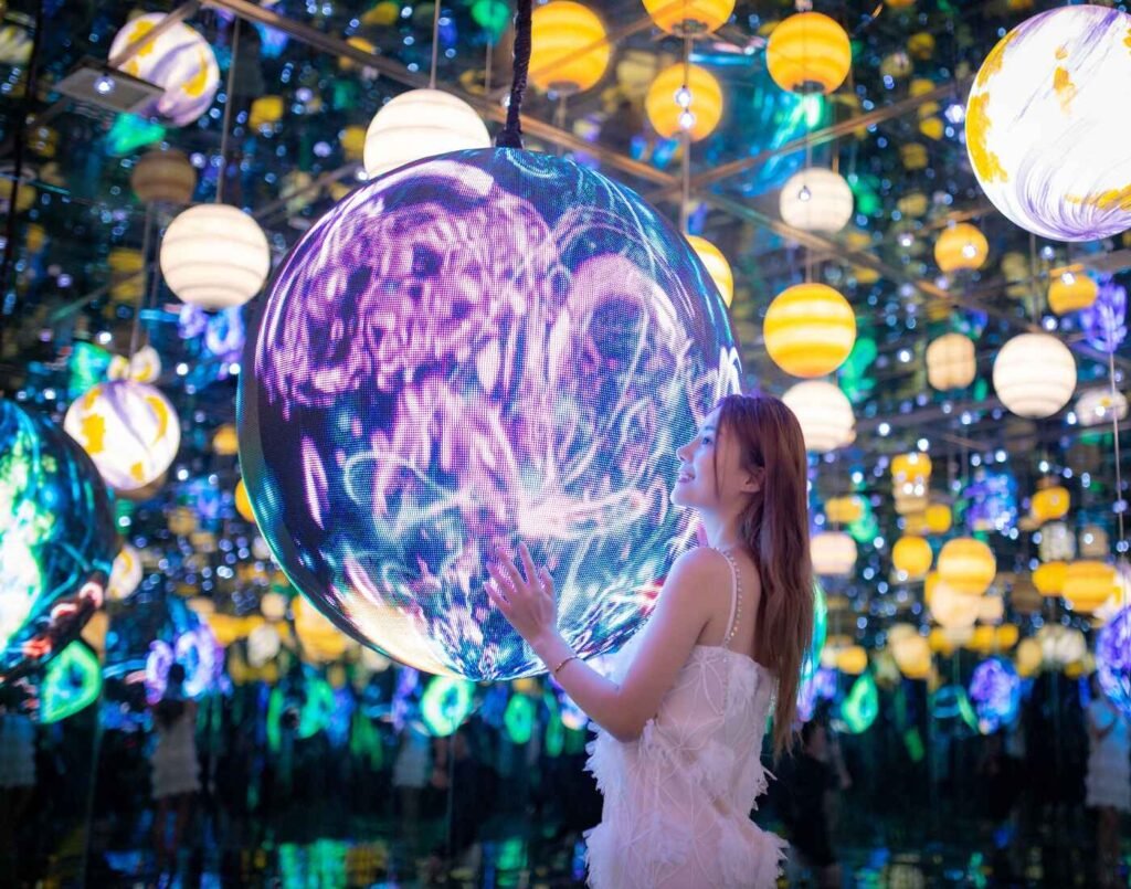 A woman admires the countless round LED lights, representing planets and stars, hanging from the ceiling, emitting a soft glow as if one were in the midst of space. This exhibit is the Wandering Planets at Space & Time Cube, The Amusement, Third Floor, Isetan The Japan Store Lot 10, Bukit Bintang, Kuala Lumpur.