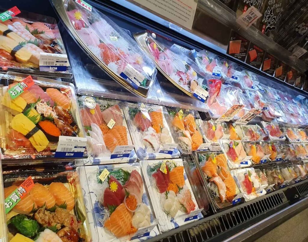 A refrigerated case displaying multiple rows of pre-packaged sets of sushi, sashimi, and various seafood at the Hirashima Seafood Tasting Bar, a crowd favourite at Hirashima Sushi, The Market, Lower Ground Floor, Isetan The Japan Store Lot 10, Bukit Bintang, Kuala Lumpur.