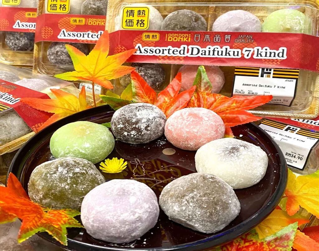 A vibrant assortment of Daifuku, traditional Japanese mochi filled with sweet bean paste, presented with autumn-themed decorations. The pack includes Matcha, Strawberry, Chocolate, Melon, Houjicha, Sweet Potato, and Original flavours in pastel shades of green, pink, white, and purple, available at Jonetz By Don Don Donki Lot 10, a Japanese supermarket in Bukit Bintang, Kuala Lumpur.