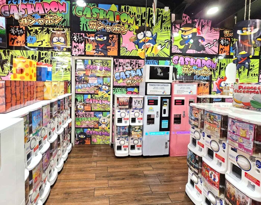 Rows of Japanese gashapon capsule toy machines on the ground floor of Don Don Donki Lot 10 featuring Bandai collectible capsules, anime characters, and miniature toys.