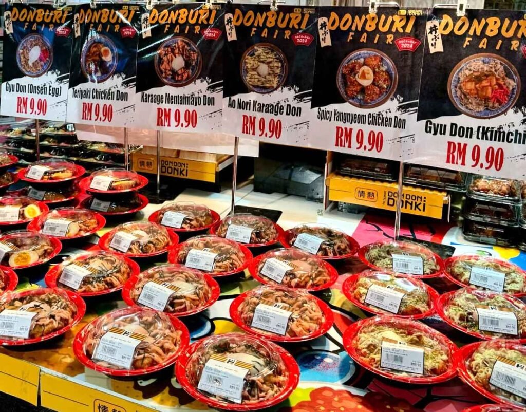 Donburi Fair featuring pre-packaged Japanese rice bowl dishes including Gyu Don (with Onsen Egg), Teriyaki Chicken Don, Karaage Mentaimayo Don, Ao Nori Karaage Don, Spicy Yangnyeom Chicken Don, and Gyu Don (with Kimchi) displayed in the ready meal section at Jonetz By Don Don Donki Lot 10, a Japanese supermarket in Bukit Bintang, Kuala Lumpur.