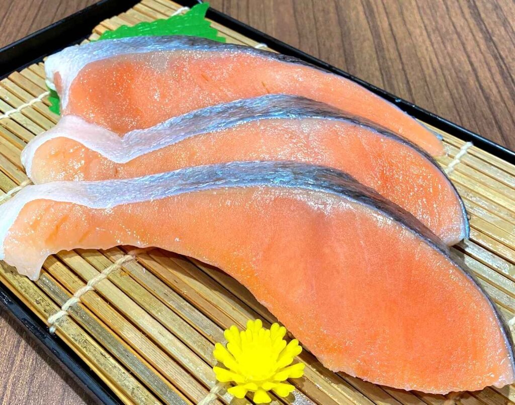 Three thick, vibrant fillet slices of fresh Silver Salmon, also known as Coho Salmon, and ginzake (銀鮭), skin-on, presented on a bamboo mat. A staple food and popular  Japanese breakfast dish, bento, or onigiri! It is rich in Omega 3 fatty acids, easy to cook and is perfect for grilling and pan-frying. Available in the seafood section of Jonetz By Don Don Donki Lot 10, a Japanese supermarket in Bukit Bintang, Kuala Lumpur.