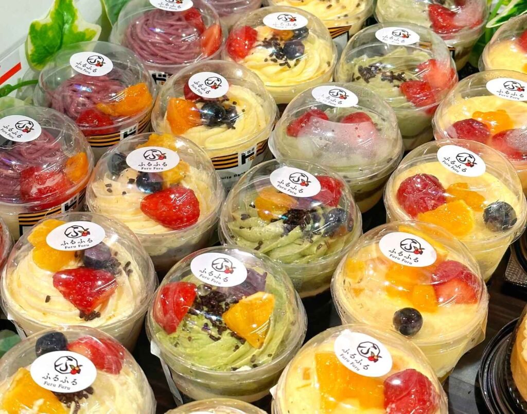Colourful Japanese fruit parfaits layered with fresh fruits like strawberries, mango, blueberry, whipped cream, jelly, and sponge cake, beautifully presented in clear cups in the chiller at the Furu Furu section, on the First Floor of Jonetz By Don Don Donki Lot 10, a Japanese supermarket in Bukit Bintang, Kuala Lumpur.