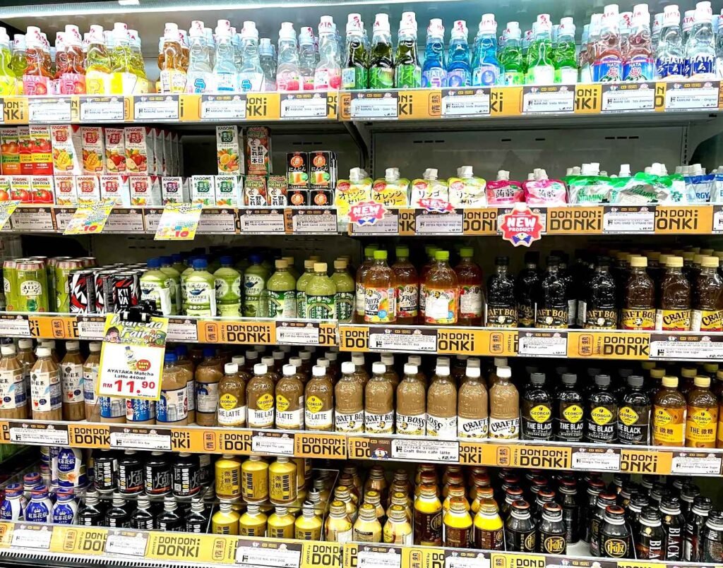 A wide assortment of imported Japanese drinks in cans, bottles, cartons, and packets, including green tea, milk tea, canned coffee, fruit juices, sports drinks, energy drinks, flavoured teas, sodas, and everyday ready-to-drink beverages from popular Japanese brands, displayed on the 1st floor of Jonetz By Don Don Donki Lot 10, a Japanese supermarket in Bukit Bintang, Kuala Lumpur.