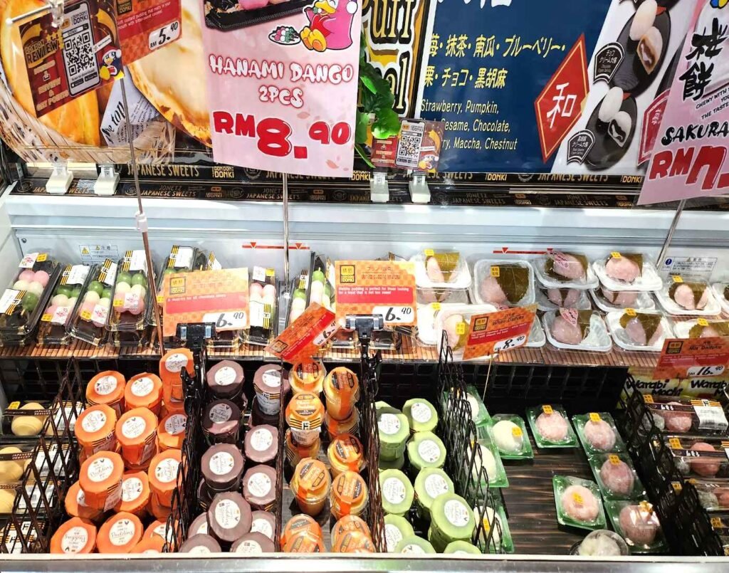 A vibrant display of traditional Japanese sweets including Hanami Dango skewers, assorted Daifuku, and Sakura Mochi, neatly arranged in the chilled wagashi section at Jonetz By Don Don Donki Lot 10, a Japanese supermarket in Bukit Bintang, Kuala Lumpur. The section showcases pastel pink, white, and green colours of mochi-based confections with price tags and store signage highlighting seasonal and limited-edition varieties.