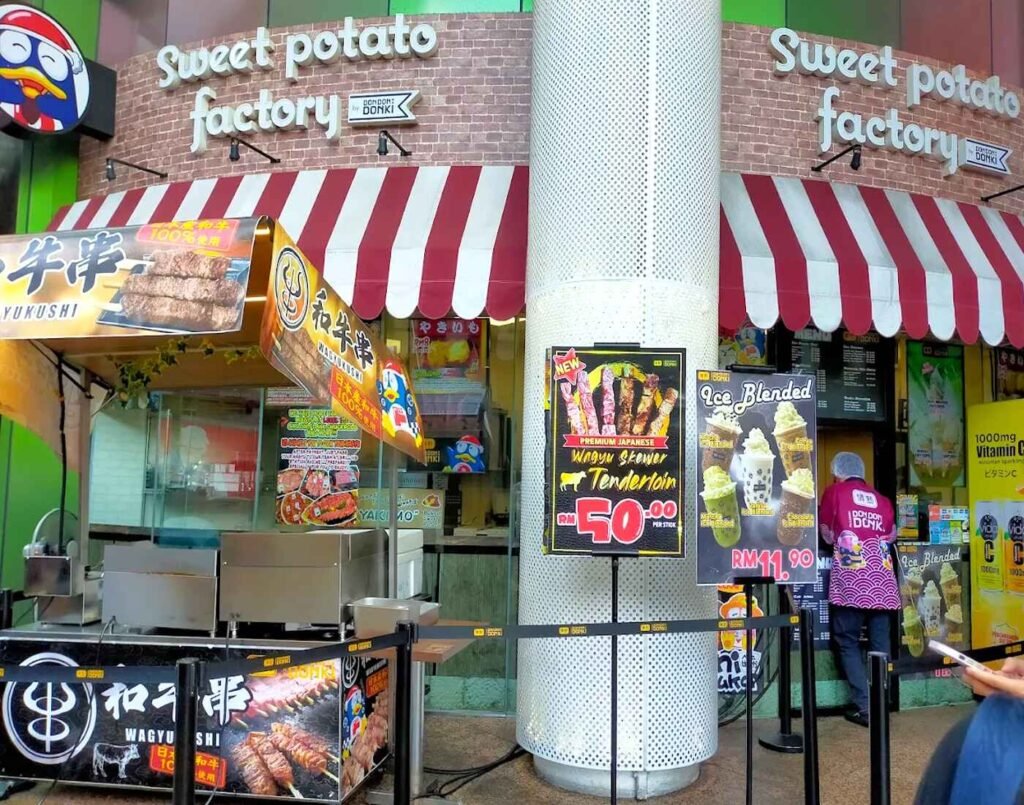Entrance view of the Sweet Potato Factory kiosk at Lot 10, showcasing its bright signage located at the main entrance of Lot 10 shopping mall, just before the ground floor entrance of Jonetz By Don Don Donki Lot 10, a Japanese supermarket in Bukit Bintang, Kuala Lumpur.