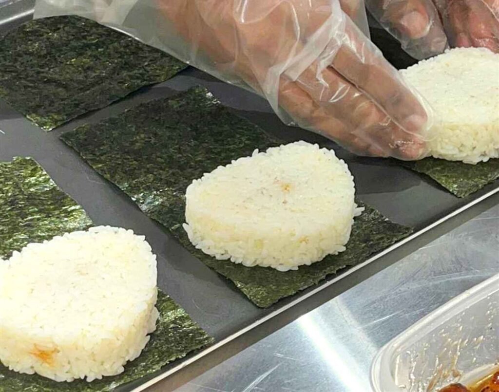 A chef prepares heart-shaped portions of freshly cooked rice on sheets of dried Nori seaweed, a step in hand-making Onigiri (rice balls) at Tomita Seimai, located on the 2nd floor of Jonetz By Don Don Donki Lot 10, a Japanese supermarket in Bukit Bintang, Kuala Lumpur.