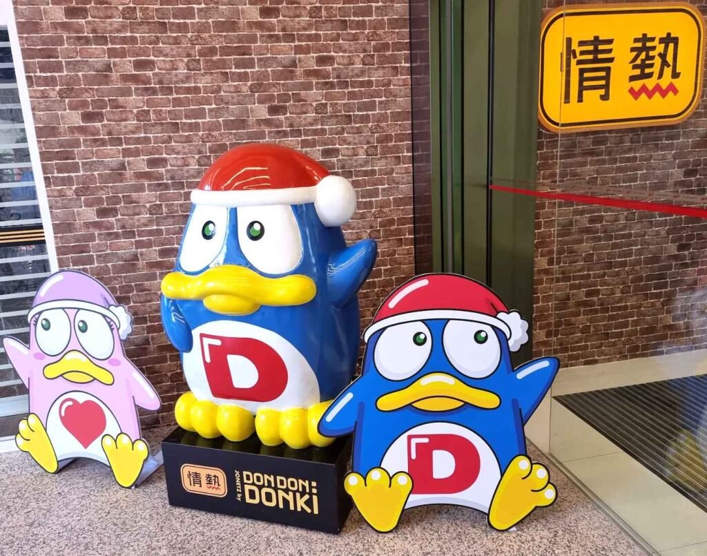 Don Pen and Don Ko mascots standing at the main entrance of JONETZ by Don Don Donki Lot 10, featuring the store's "Passionate Price" logo.