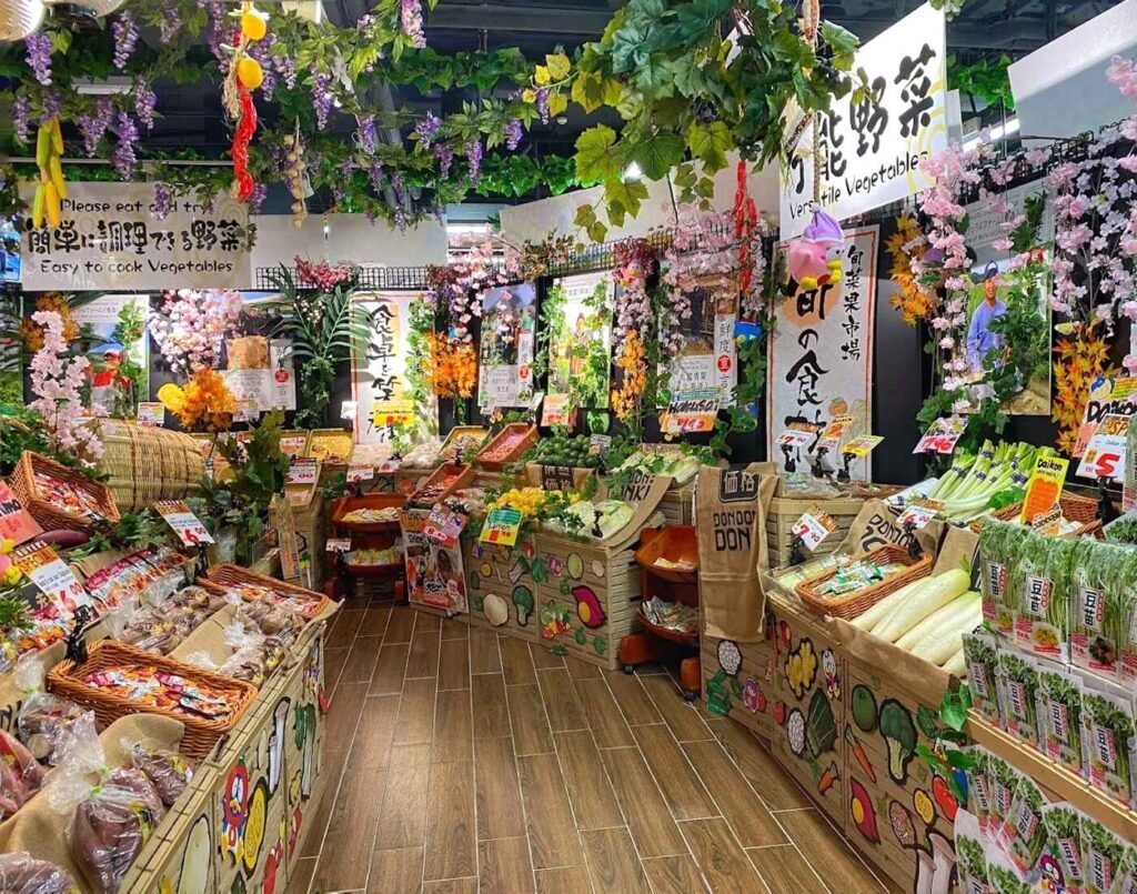 The Furu Furu fresh produce section featuring a variety of imported Japanese vegetables like daikon, sweet potatoes, and leafy greens under colorful floral decorations at Jonetz By Don Don Donki Lot 10, a Japanese supermarket in Bukit Bintang.