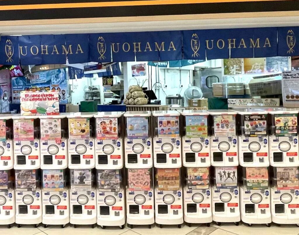 A row of white Gashapon capsule toy vending machines located adjacent to the Uohama Live Kitchen at the 2nd floor entrance of JONETZ by Don Don Donki Lot 10 in Bukit Bintang.